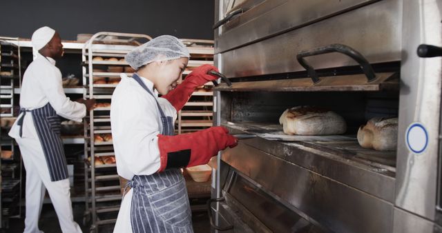 Bakers preparing fresh bread in commercial kitchen, using professional equipment including industrial ovens. Can be used for content related to baking, commercial kitchens, food industry, teamwork in culinary arts, bread preparation, or culinary education.