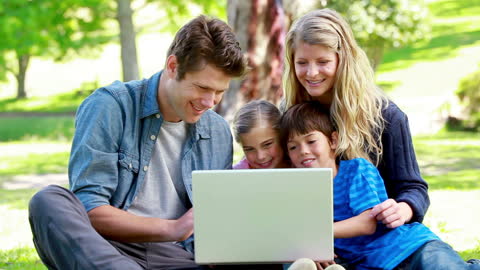Happy Family Laughing Together While Using Laptop Outdoors