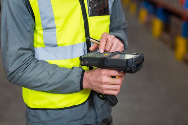Mid section of warehouse worker using barcode scanner machine in warehouse