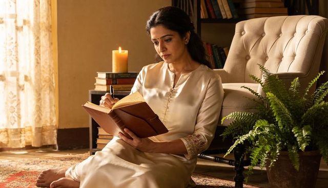 Woman writing in leather journal on vintage rug beside candlelit stack of books