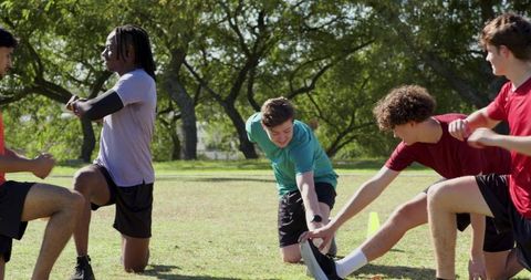 Multiracial male athletes doing dynamic warmup and partner stretching in park