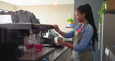 African american barista steaming milk and pouring latte at espresso machine, minimalist cafe
