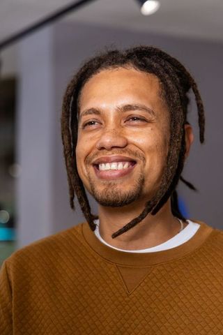 Smiling african american man with dreadlocks wearing brown quilted sweatshirt in gallery