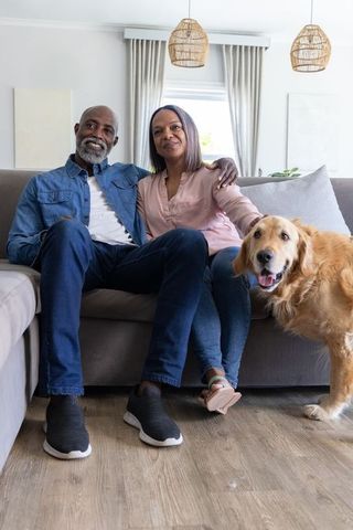 Mature couple sitting on sofa with golden retriever in bright modern living room