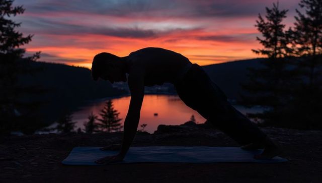 Silhouette of man practicing plank pose by lake at sunset