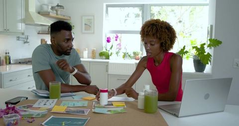 Black couple planning health supplement startup in bright kitchen workspace