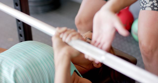 Woman performing a bench press at a gym, receiving assistance from a personal trainer. Excellent for websites and advertisements about fitness, personal training services, gym memberships, exercise routines, and strength training guides.