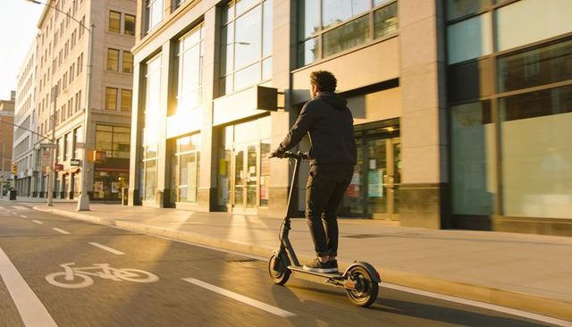 Commuter riding electric scooter along urban bike lane at golden hour
