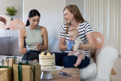 Mother and Friend Preparing Birthday Cake with Gifts and Baby
