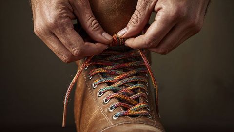 Tying colorful braided laces on brown leather boot showing hands and metal eyelets