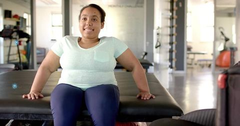 Smiling woman sitting on therapy table placing hands for rehab session in clinic gym
