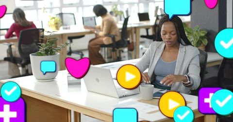 Black businesswoman typing on laptop in modern coworking space with social media icons