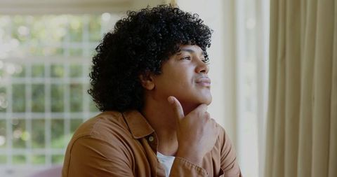 Smiling Man with Curly Hair Contemplating by a Window Indoors