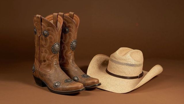 Cowboy boots with concho decoration and straw hat on table