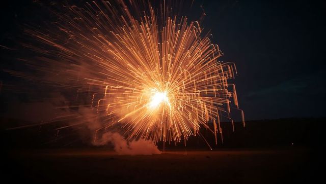 Golden Firework Explosion Illuminating Night Sky Over Field