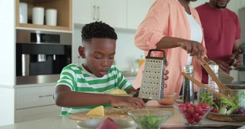 African american family preparing meal boy grating cheese on modern kitchen island