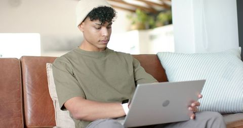 African American Young Man Working on Laptop on Couch Wearing Beanie and Smartwatch