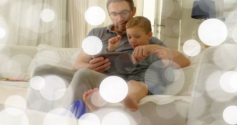 Parent bonding with child using tablet on cozy pale sofa in home living room with bokeh