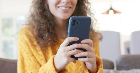 Young woman smiling and texting on smartphone in cozy mustard sweater
