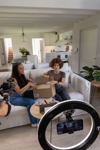 African american creators filming unboxing video on sofa with ring light and camera gear