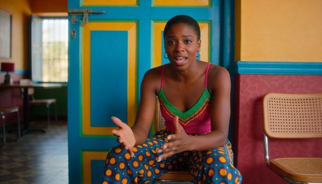 Woman speaking and gesturing in colorful cafe with patterned pants and teal door