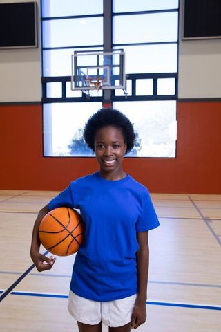 Teenage Girl Smiling with Basketball in School Gymnasium