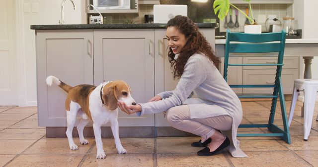 A young African American woman is engaging with a beagle dog in a bright kitchen setting, with copy space. Her gentle interaction with the pet adds a warm, homely atmosphere to the image.