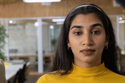 Indian woman wearing mustard top looking at camera in modern coworking office