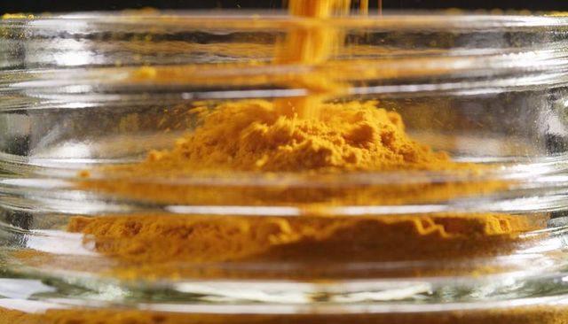 Pouring turmeric powder forming golden mound inside ridged glass jar macro close-up