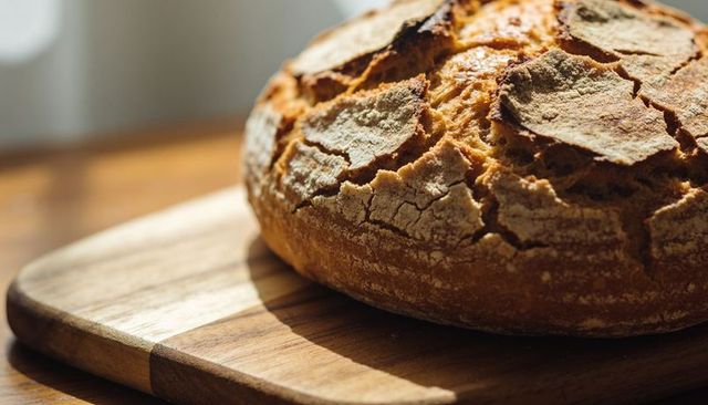 Sunlit rustic sourdough loaf on wooden cutting board with cracked golden crust