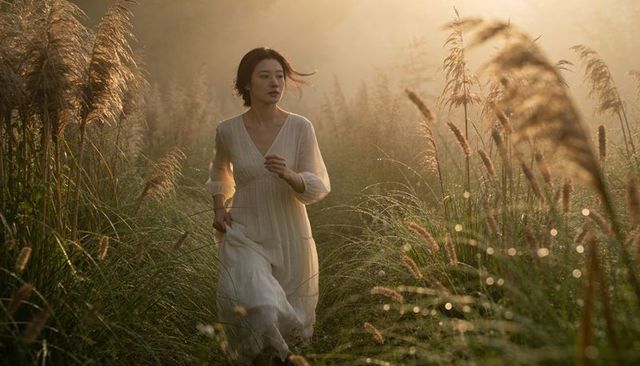 Asian woman walking through misty reed meadow at golden hour in flowing white dress