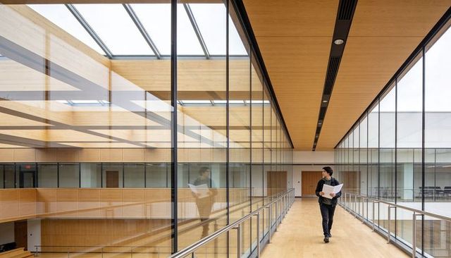 Student Walking on Glass-Walled Campus Bridge Holding Papers in Modern Atrium