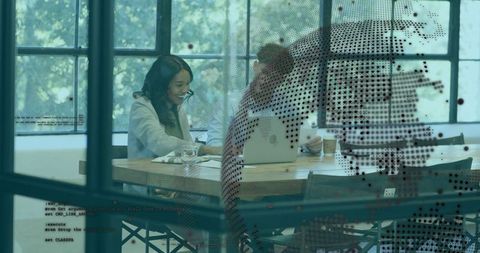 Professionals collaborating over laptop and documents in coworking office with dotted glass
