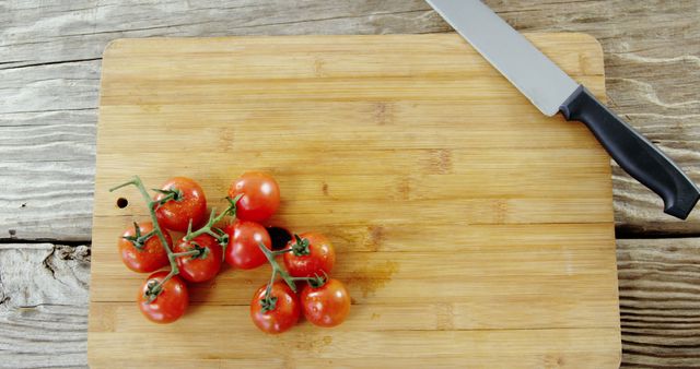 A cluster of ripe cherry tomatoes lies next to a kitchen knife on a wooden cutting board, with copy space. Perfect for culinary themes, the image evokes fresh ingredients and meal preparation.