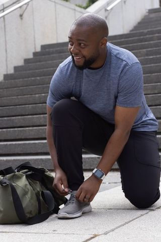 African man tying running shoes on urban steps preparing for outdoor workout and training