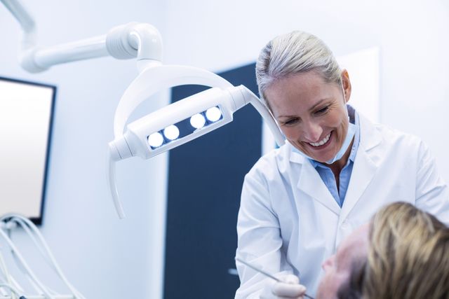 Dentist examining patient with dental tools in a modern clinic. Ideal for use in healthcare, dental care, and medical service promotions. Can be used in brochures, websites, and advertisements related to dental health and hygiene.