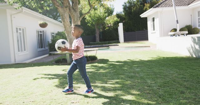 Image portrays young boy playing with a soccer ball in a suburban backyard on a bright afternoon. Perfect for themes related to childhood, outdoor activities, active lifestyle, residential living, and family life. Can be used for advertising family-oriented services, recreational products, or home and garden articles.