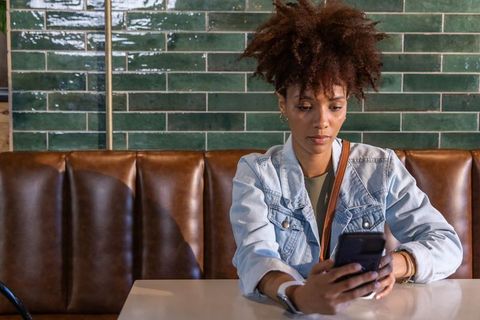 African american woman using smartphone while sitting in modern cafe booth