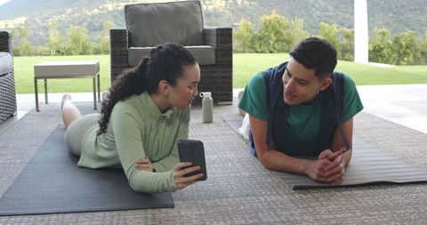 Couple relaxing on yoga mats with smartphone in outdoor, natural setting