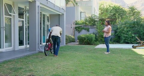 Father Teaching Son to Ride Bicycle in Backyard on Sunny Day