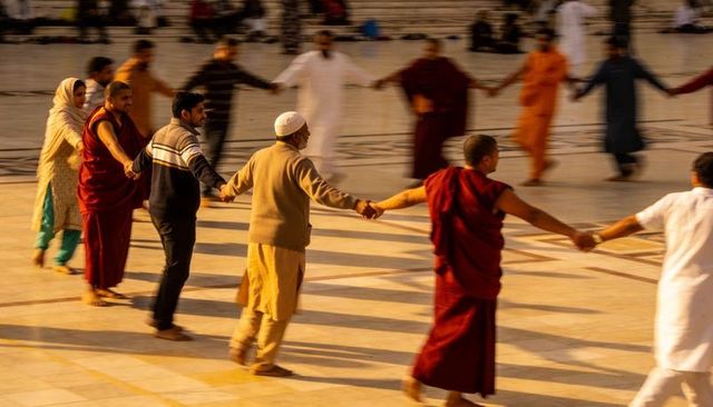 Interfaith community holding hands in circular ritual on marble courtyard at sunset