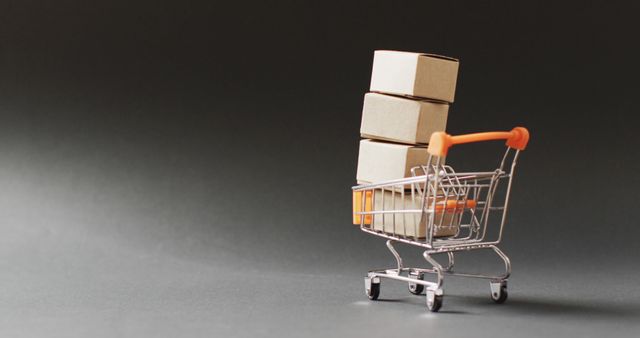 Mini shopping cart filled with small cardboard boxes placed on a dark background. Ideal for illustrating concepts related to online shopping, e-commerce, delivery, logistics, and retail industries. Can be used in marketing materials, blog posts, or websites focusing on consumerism, packaging, and shipping.