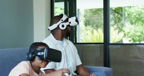 African American Father and Teen Son Bonding Through Virtual Reality Gaming on Couch