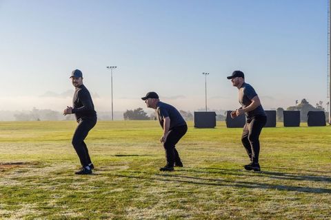 Mature Football Teammates Practicing Defensive Stances on Dewy Field With Training Pads