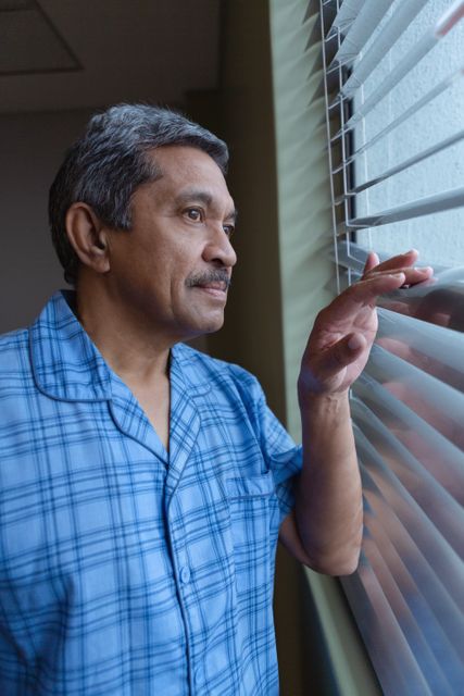 Side view of mature male patient looking through window in hospital