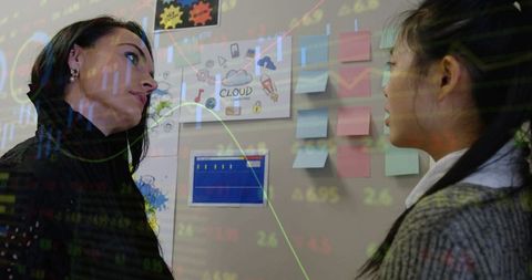 Two female colleagues reviewing data and sticky notes during cloud project brainstorming