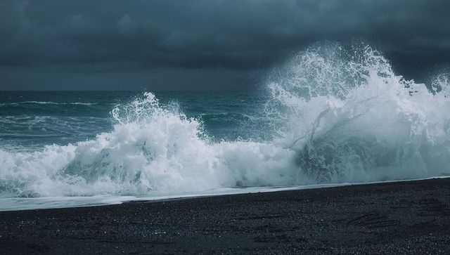 Storm waves crashing on black sand beach under dark cloudy sky