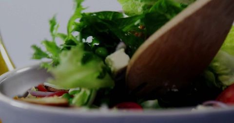 Tossing Fresh Green Salad with Wooden Spoon in Kitchen