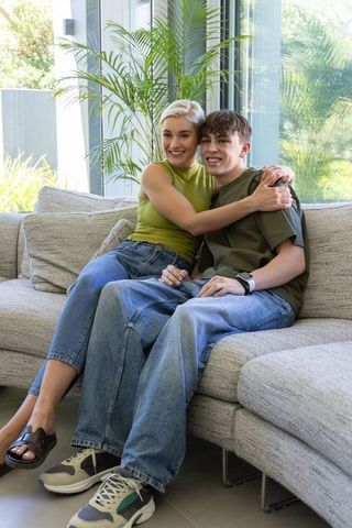 Mother hugging teenage son on gray sectional couch in bright modern living room