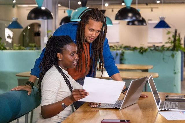 African American Team Collaborating Over Laptop and Documents in Coworking Hub